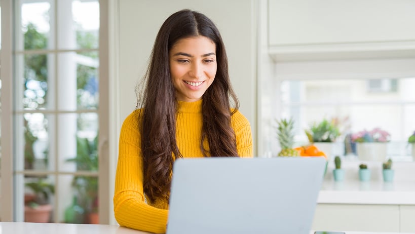 Woman in yellow sweater types on laptop