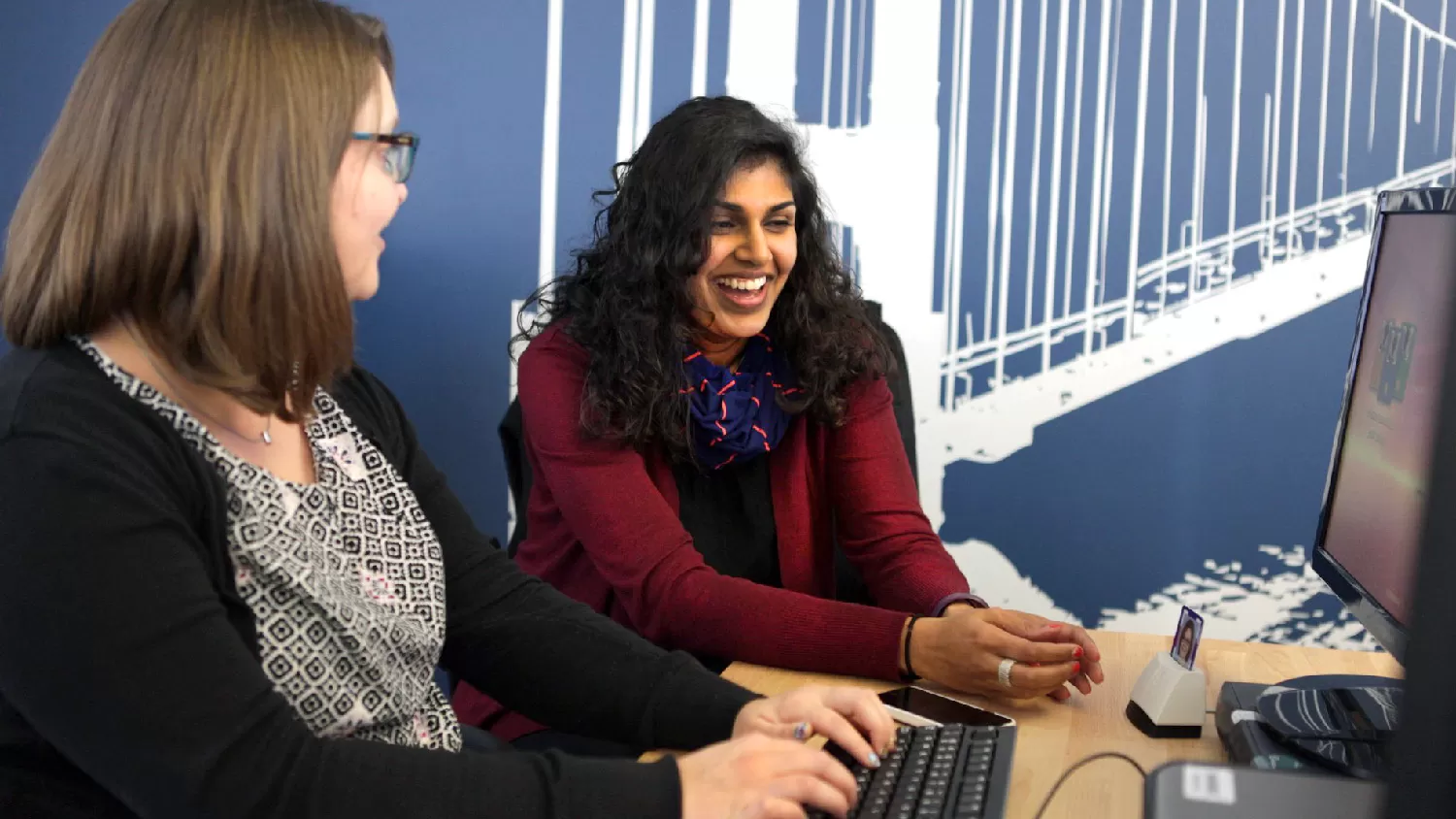 Two female employees smiling and looking at a computer screen