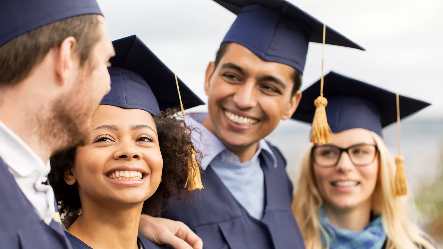 Four students looking at each other smiling at their graduation ceremony