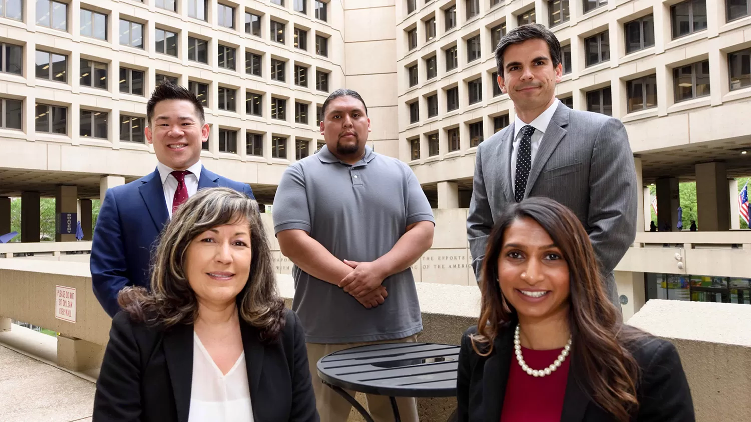 A group of diverse people looking at the camera while sitting in the FBI Courtyard