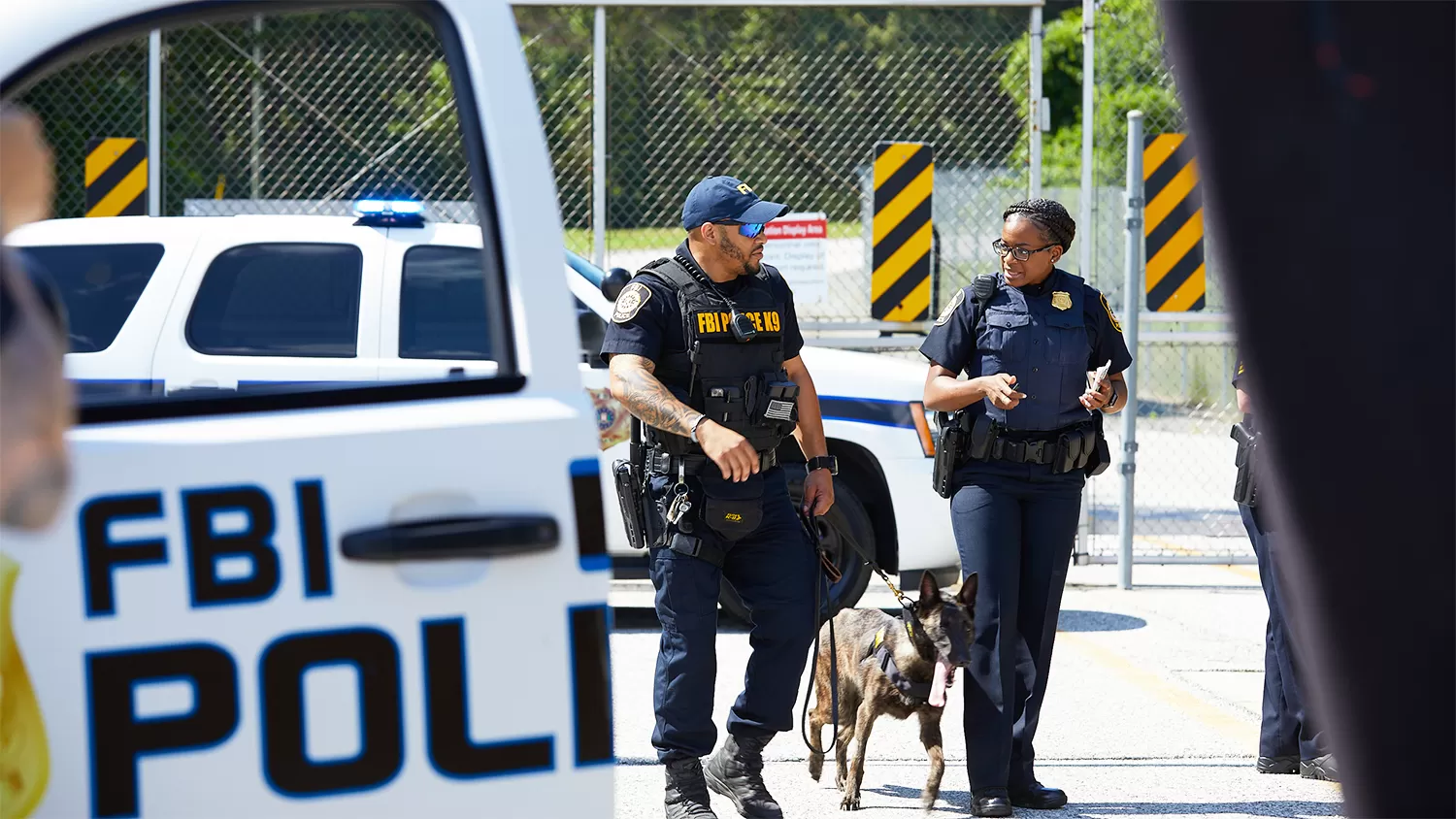 Two FBI police officers and their dog talking in front of their police vehicle