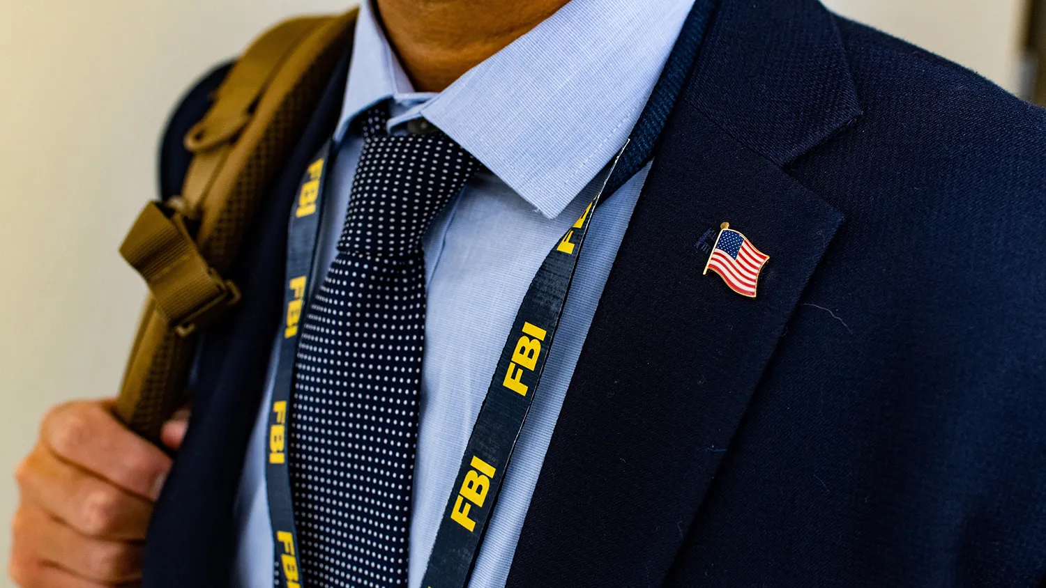 Close up of FBI lanyard and American flag pin, with military backpack in the background.